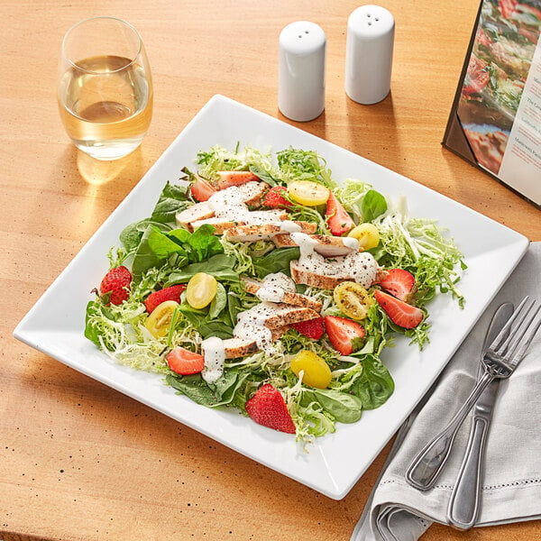 A white square Acopa porcelain plate with a salad, meat, strawberries, and cheese.