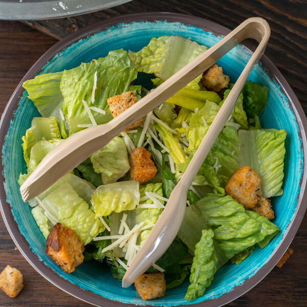 A bowl of salad with Carlisle beige plastic salad tongs.