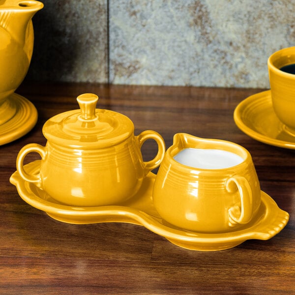 A yellow Fiesta sugar and creamer tray set on a wooden surface.