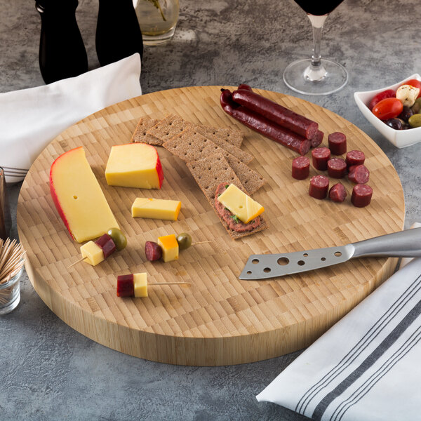 An American Metalcraft bamboo cutting board with cheese and sausages on a table.