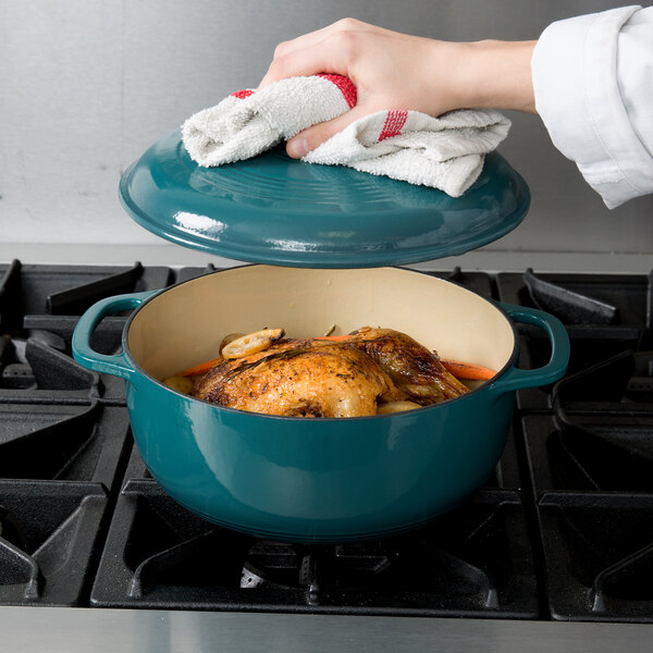 A woman using a Lodge lagoon enameled cast iron Dutch oven to cook chicken on the stove.