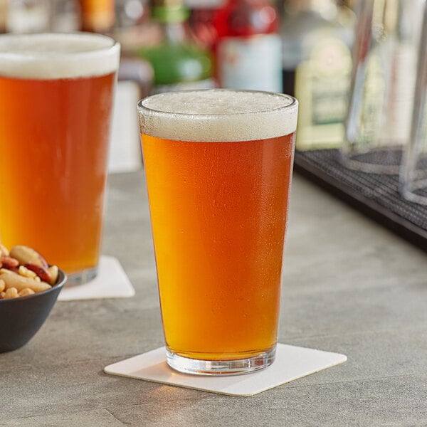 Two Acopa pint glasses of beer on a table with a bowl of nuts.
