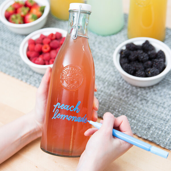 A person using a Franmara neon blue mini tip glass marker to write on a bottle of juice.