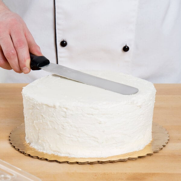 A person using an Ateco straight baking / icing spatula with a black plastic handle to cut a cake.