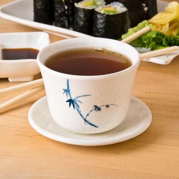 A Thunder Group Blue Bamboo melamine tea cup filled with brown liquid on a table with sushi.