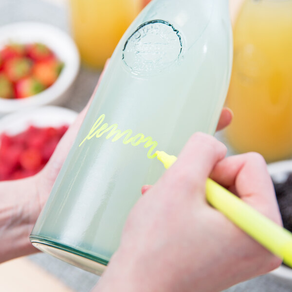 A person using a Franmara neon yellow mini tip marker to write on a glass bottle.