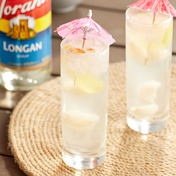 A glass of Torani Longan flavored liquid with ice and a pink and white straw.
