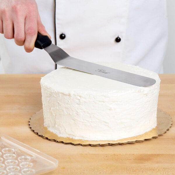 A person using an Ateco offset baking spatula to cut a cake.