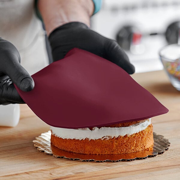 A person wearing black gloves cutting a Satin Ice burgundy cake.