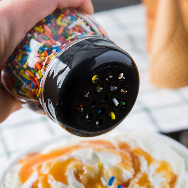 A hand holding a Tablecraft black shaker with sprinkles over a cup of ice cream.