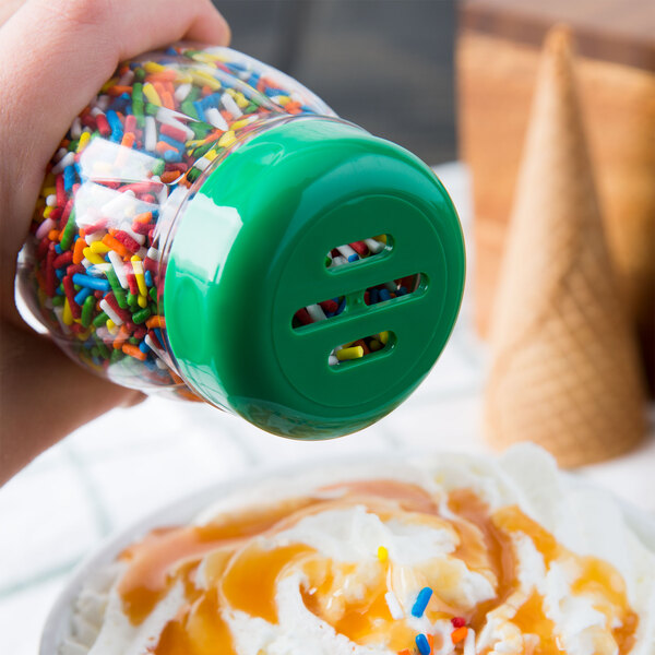 A hand using a Tablecraft green plastic slotted shaker top to sprinkle sprinkles on ice cream.