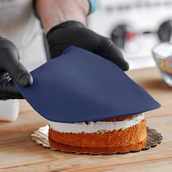 A person wearing black gloves rolling navy Satin Ice fondant over a cake.