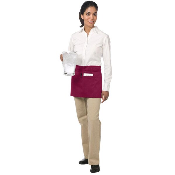 A woman wearing a burgundy Chef Revival waist apron holding a glass of ice.