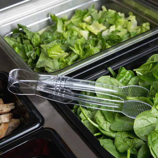 Clear plastic tongs being used to serve salad at a salad bar.
