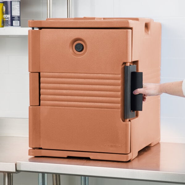 A person opening a brown Cambro Ultra Pan Carrier door with a handle.