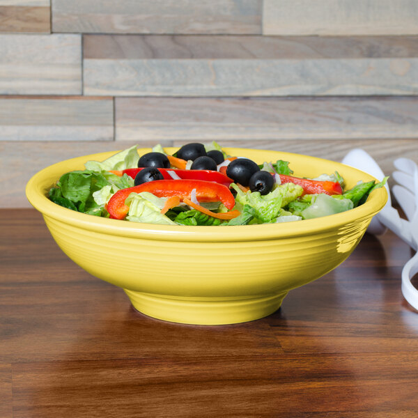 A Fiesta Sunflower china pedestal serving bowl filled with salad on a table.