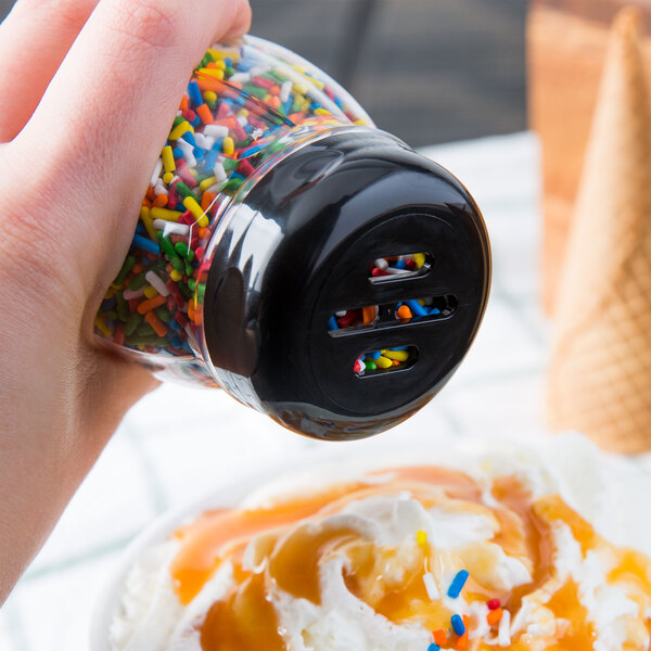 A hand using a Tablecraft black plastic slotted shaker top to sprinkle sprinkles on a cup of ice cream.