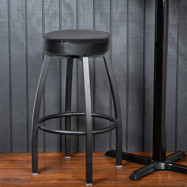 A Lancaster Table & Seating black swivel backless bar stool with a black vinyl seat and metal base.