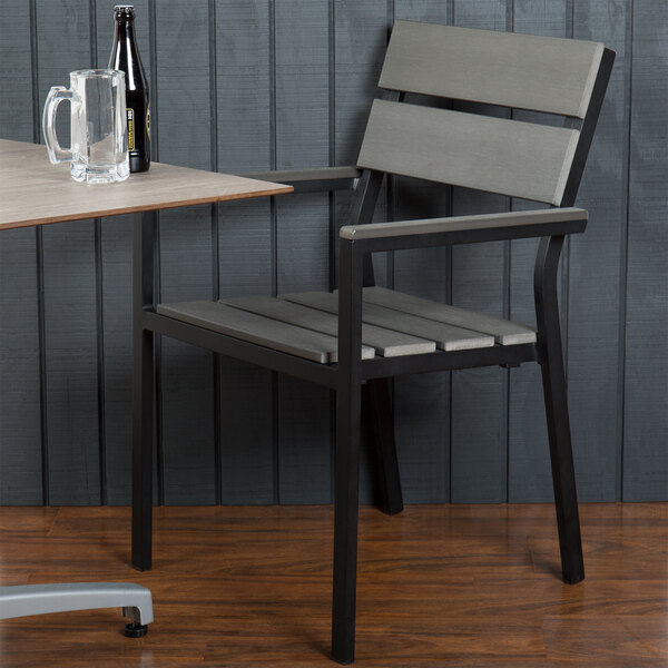 A BFM Seating black aluminum armchair with a gray synthetic teak back and seat next to a table with a beer bottle and a glass on it.