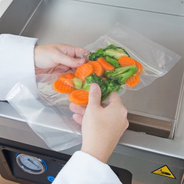 A person holding a VacPak-It chamber vacuum packaging bag of vegetables.