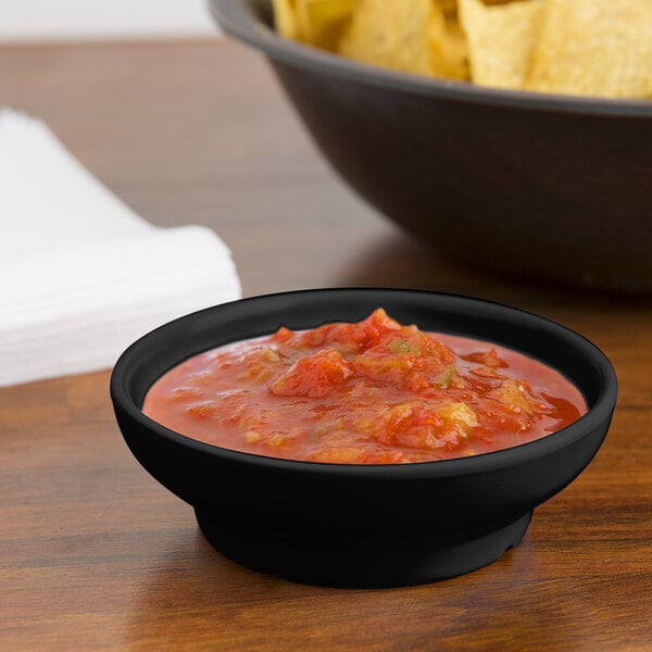 A black melamine salsa dish filled with salsa next to a bowl of chips.