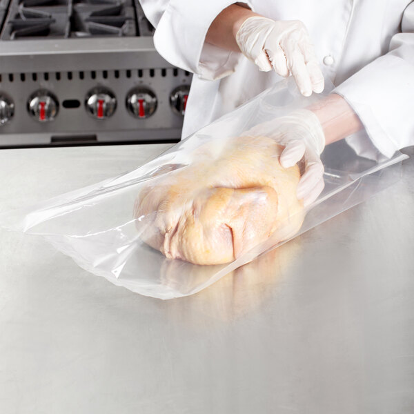 A person in white gloves using a VacPak-It chamber vacuum packaging bag to package a raw chicken.