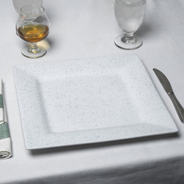 A white square porcelain charger plate with a knife on it.
