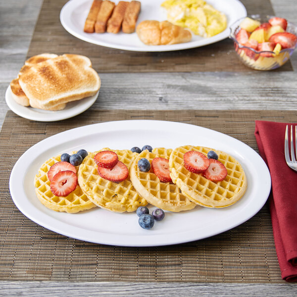 A white Thunder Group Nustone melamine oval platter with waffles, strawberries, and blueberries on a table.