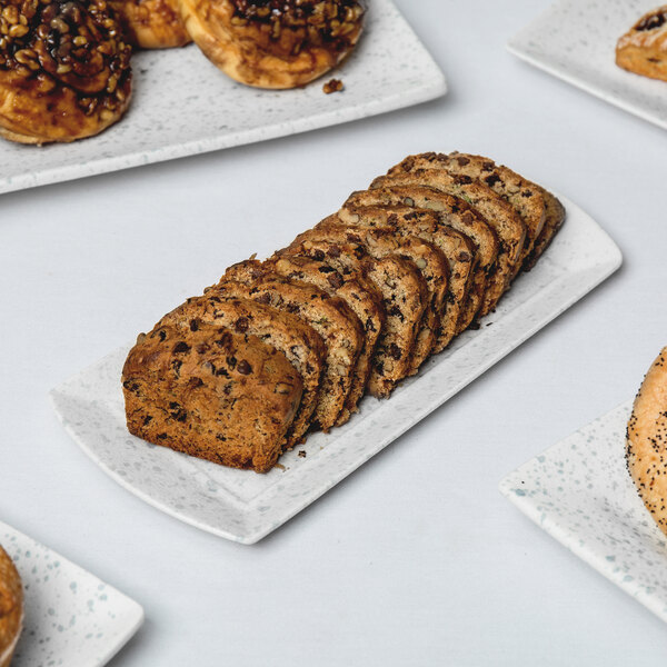 A rectangular blue speckled porcelain platter filled with a variety of breads and cookies on a white table.