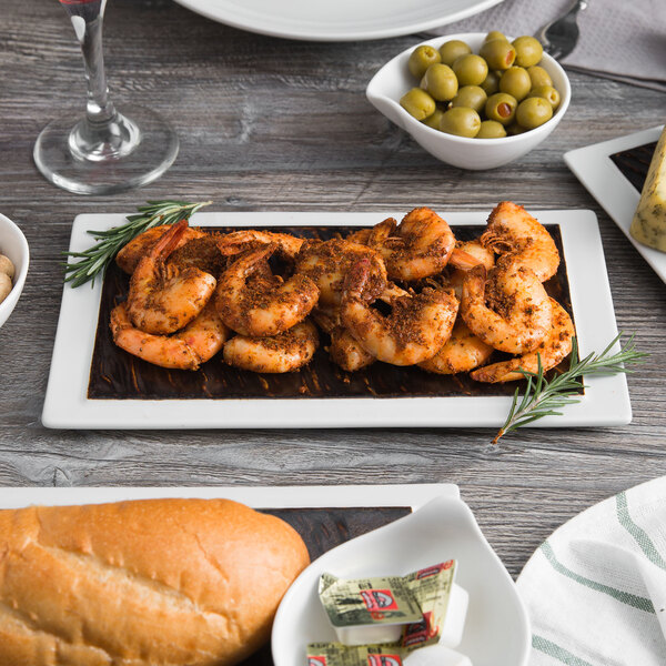 A white Tuxton rectangular plate with shrimp and bread on a table.
