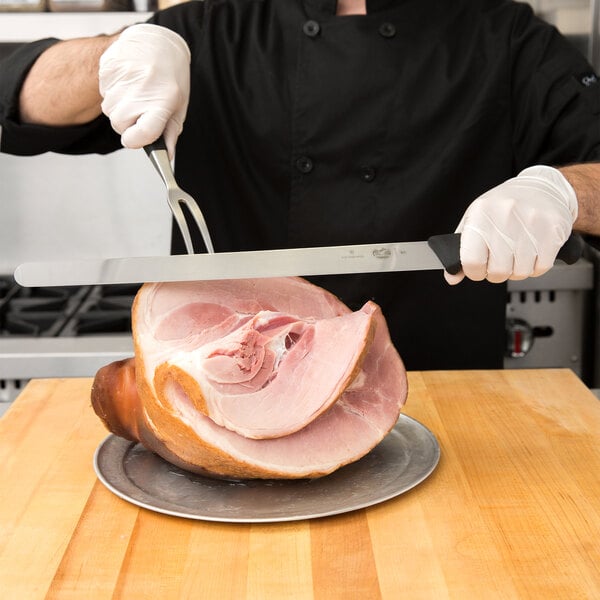 A chef using a Victorinox slicing knife to cut ham on a cutting board.