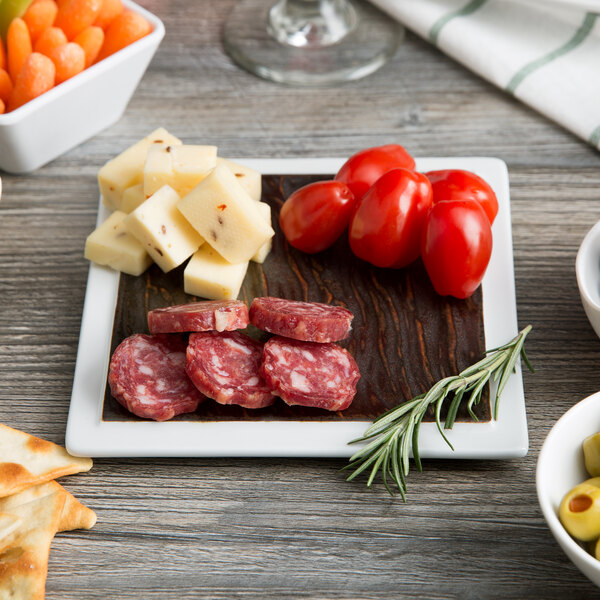 A Tuxton TuxTrendz square plate with meat, cheese, olives, and crackers on a table.