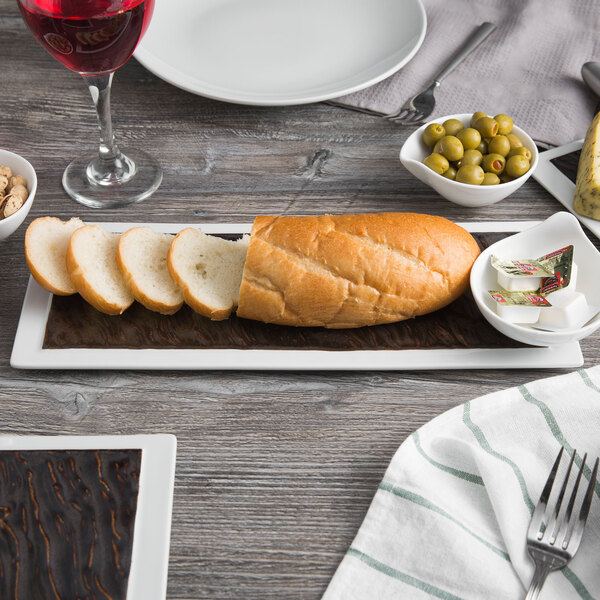 A Tuxton rectangular plate with food on it, a fork, and a glass of red wine on a table.