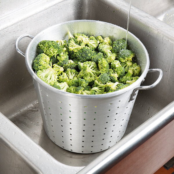A Town aluminum colander filled with broccoli in a sink.