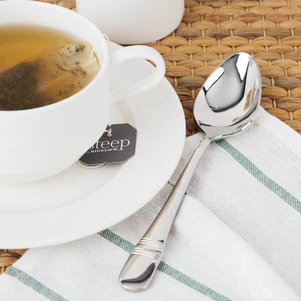 A cup of tea on a plate with a Oneida Astragal stainless steel teaspoon.