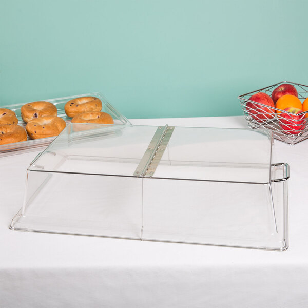 A clear glass Cambro display cover with a hinged lid on a table with food.