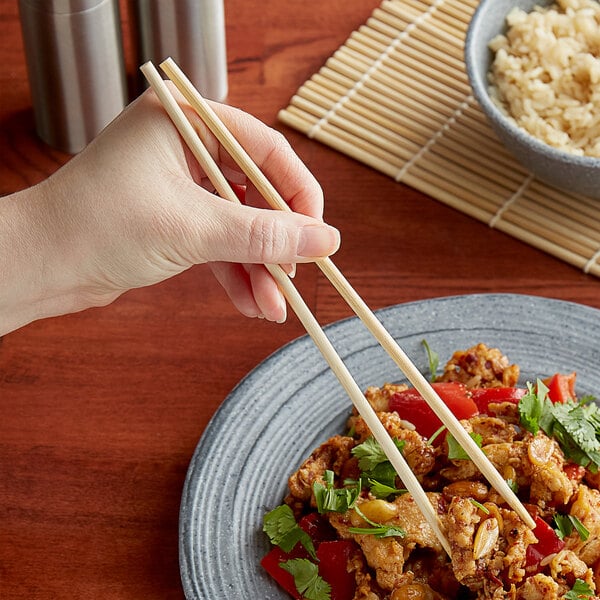 A person holding Kari-Out Company bamboo chopsticks over a plate of food.