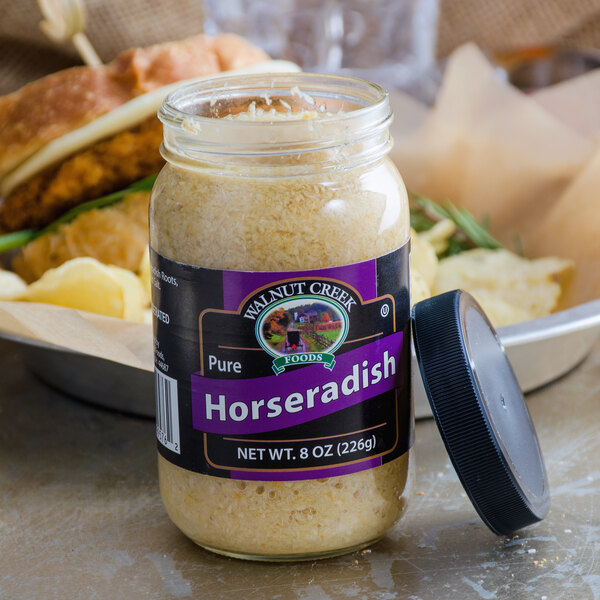 A jar of Walnut Creek Foods Pure Horseradish on a table next to a sandwich.
