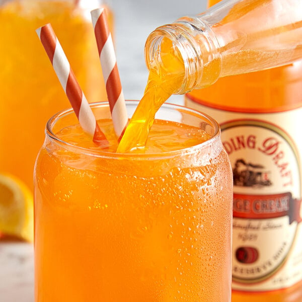 A glass bottle of Reading Soda Works Orange Cream pouring orange liquid into a glass.