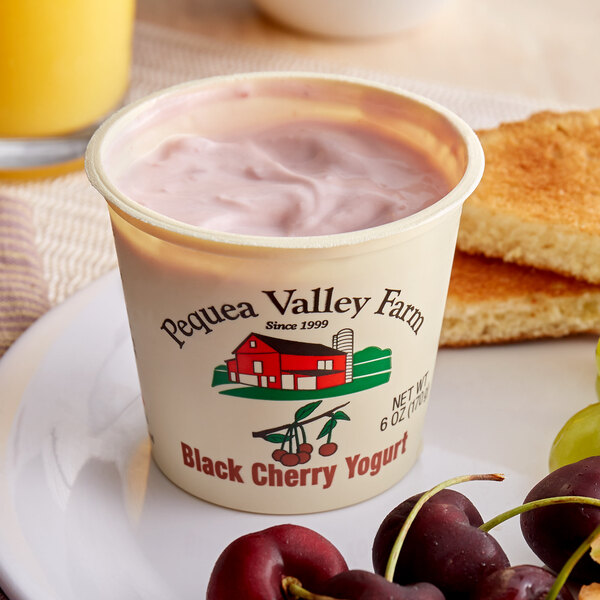 A cup of Pequea Valley Farm black cherry yogurt with fruit on a plate.