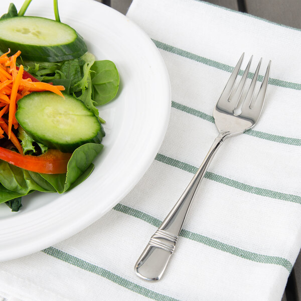 A Oneida Astragal stainless steel salad fork on a table with a plate of salad with cucumbers and carrots.