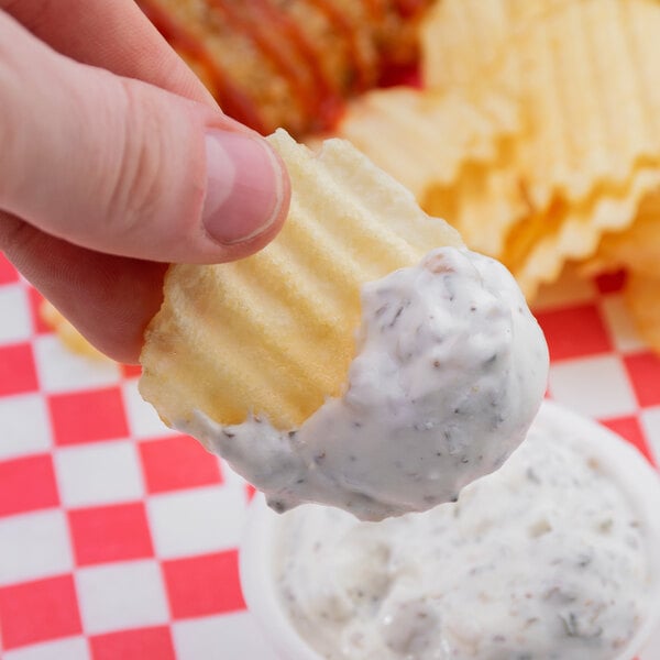 A close-up of a finger holding a Martin's Waffle Cut Potato Chip with dip.
