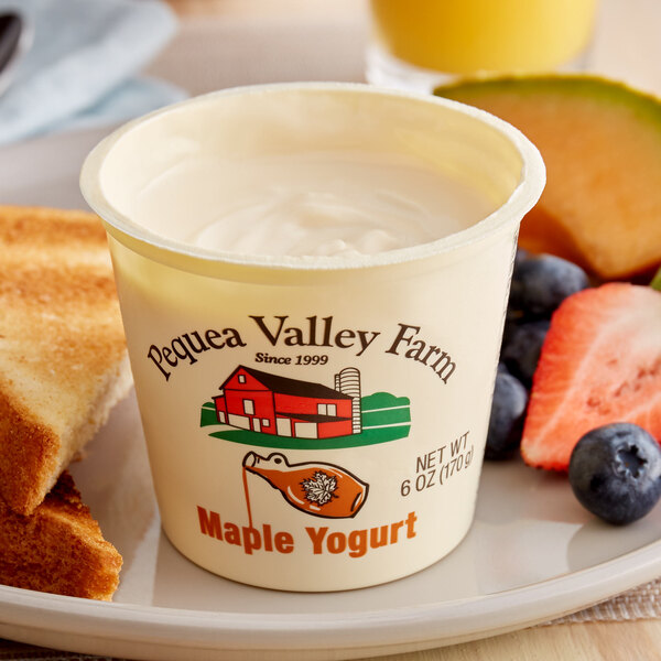 A cup of Pequea Valley Farm maple yogurt with fruit on a plate.