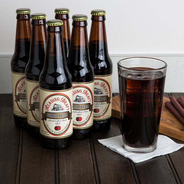 A group of Reading Soda Works Birch Beer bottles next to a glass of brown liquid.