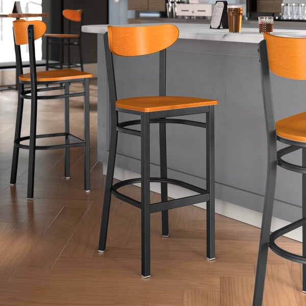 A group of Lancaster Table & Seating black bar stools with cherry wood seats and backs at a restaurant counter.