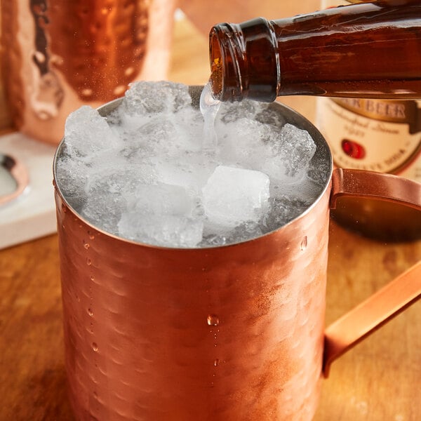 A bottle of Reading Soda Works Ginger Beer pouring into a copper mug of ice.