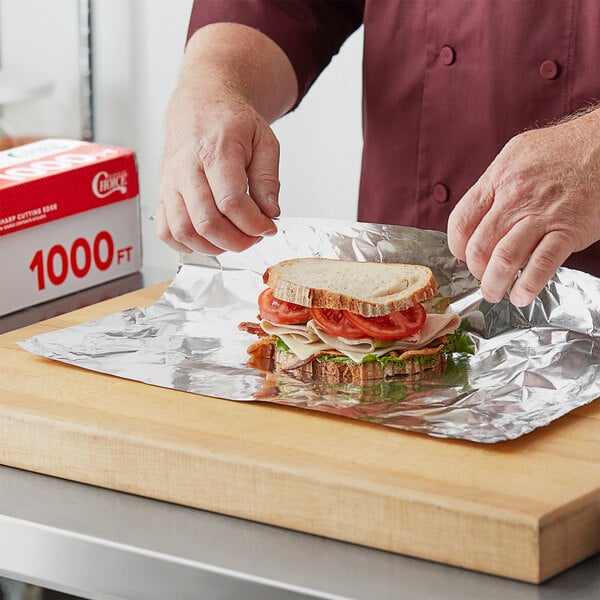 A person putting a sandwich on a sheet of Choice aluminum foil.