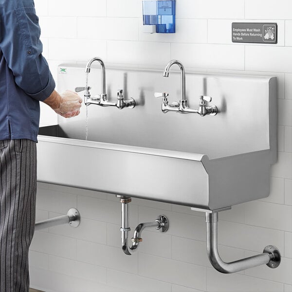 A man in a blue shirt washing his hands in a Regency multi-station utility sink.