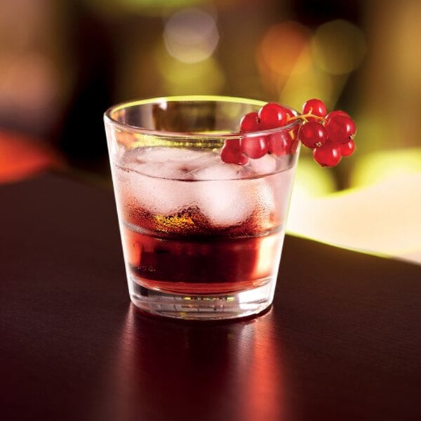 A close-up of an Arcoroc Rocks glass filled with a brown drink and ice and berries.