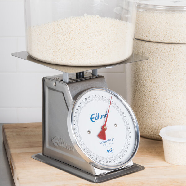 An Edlund heavy-duty receiving scale on a counter weighing a plastic container of rice.